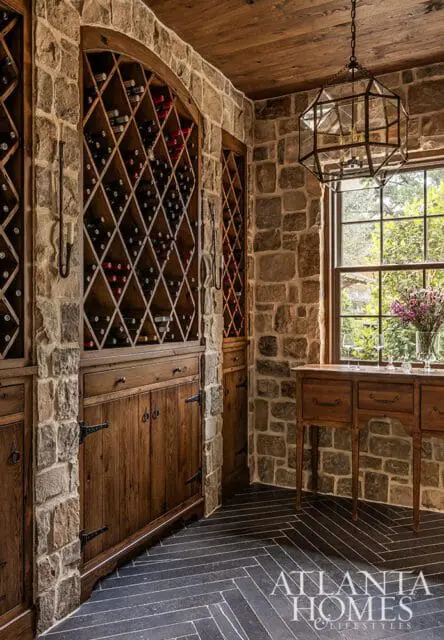 Stone wine cellar with diamond-shaped wine racks, wooden cabinets, and a glass lantern chandelier.