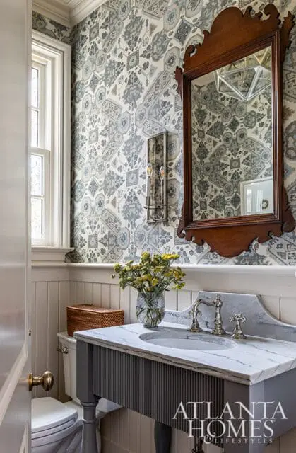 Powder room with patterned wallpaper, marble vanity, and wood mirror.