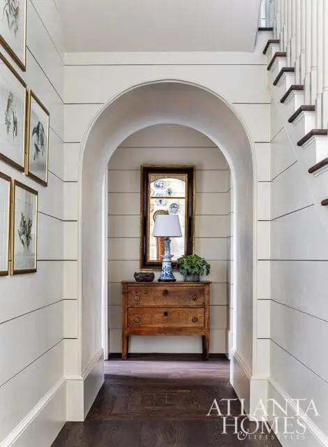 Hallway with shiplap walls, arched doorway, antique dresser, mirror, and staircase