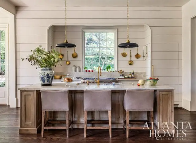Kitchen island with marble countertop, three taupe bar stools, and shiplap walls.