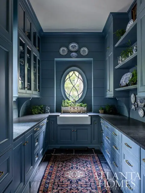Blue kitchen with farmhouse sink, oval window, and patterned rug