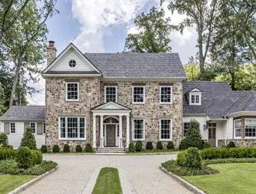 Stone and white clapboard house with gray shingle roof and manicured lawn.