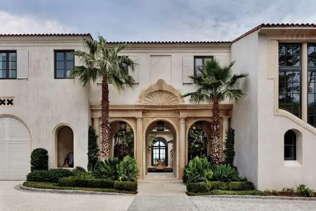 Mediterranean style home with stucco exterior, arched entryway, and palm trees.