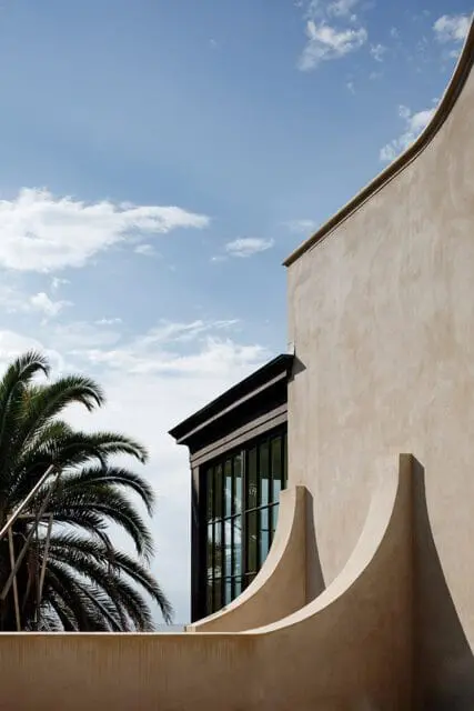 Modern building exterior with curved stucco walls, dark framed windows, and palm tree.