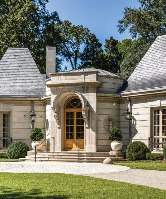 Stone mansion with arched wooden double doors, slate roof, and manicured landscaping.