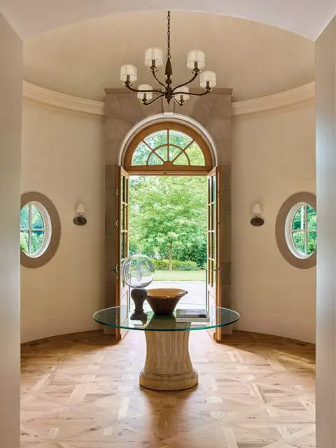 Foyer with arched doorway, glass table with decorative objects, and parquet flooring.
