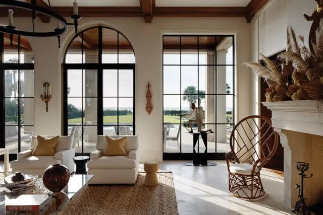 Living room with white chairs, arched windows, and fireplace. View of ocean and palm trees.