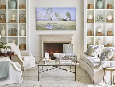 Living room with fireplace, built-in bookshelves, white slipcovered furniture, and artwork above