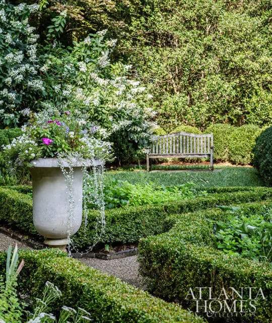 Stone urn overflowing with flowers, wooden bench in a manicured garden