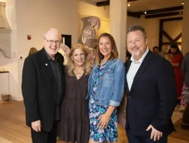 Two couples smiling at the camera in an indoor setting with artwork in the background.