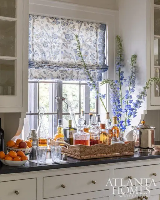 Bar cart with decanters and bottles, fruit bowl, and blue flowers
