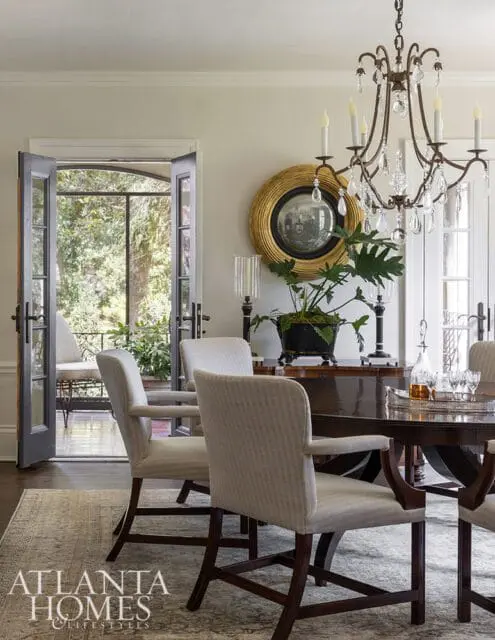 Dining room with upholstered chairs, dark wood table, ornate chandelier, and French doors opening