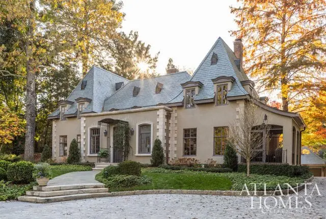 French-style home with tan stucco, gray slate roof, and stone accents.