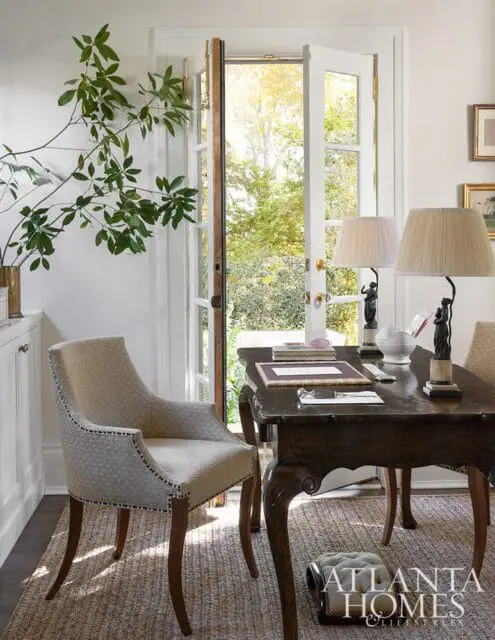 Office with upholstered chair, dark wood desk, and double doors opening to garden.