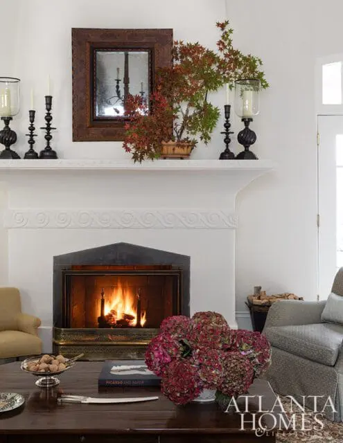 Living room fireplace with a fire burning, a mirror above the mantel, and a floral arrangement on