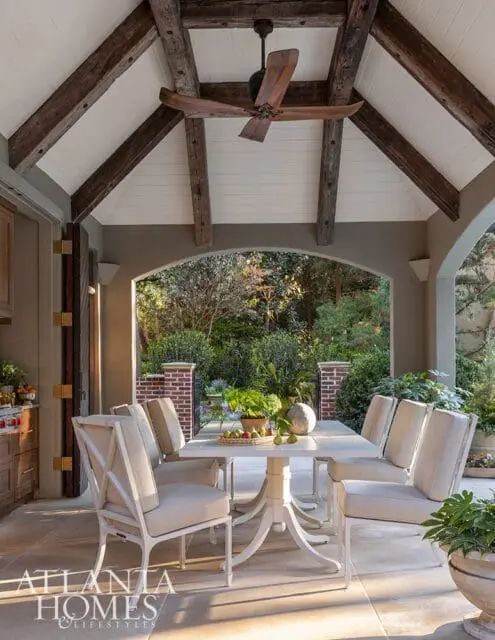 Covered patio with white dining set, ceiling fan, and arched view of garden