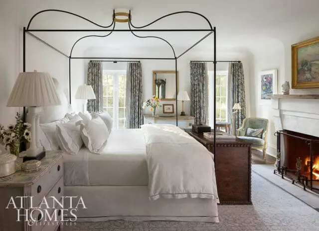 Primary bedroom with a black canopy bed, white bedding, patterned curtains, and a fireplace.