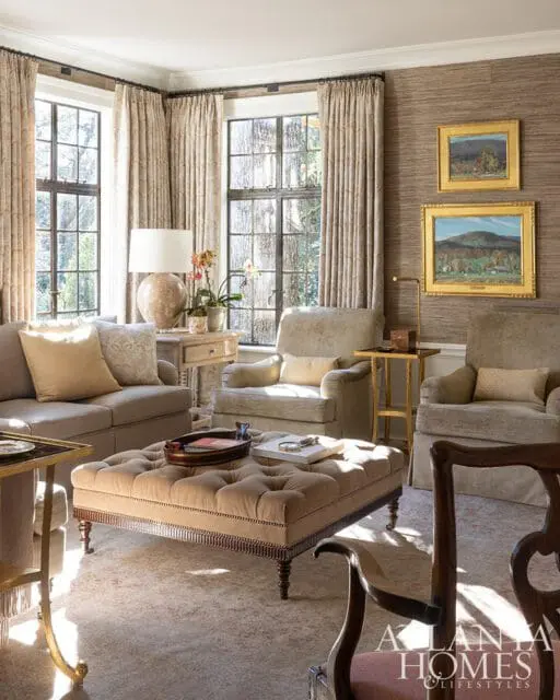 Living room with tufted ottoman, upholstered chairs, and patterned curtains.