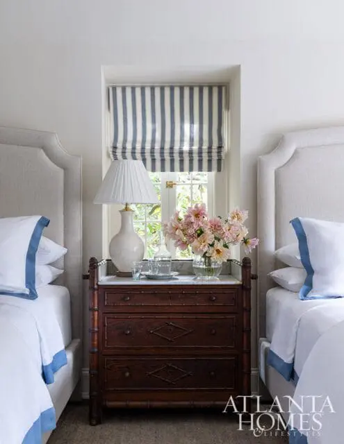 Bedroom with two beds, striped Roman shade, and antique dresser with marble top.