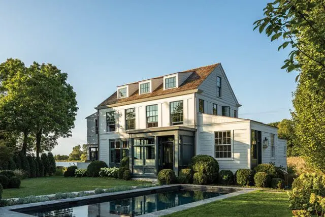 Light gray house with dormer windows and a dark gray sunroom addition next to a pool.