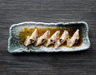 Five pieces of raw fish with black caviar and gold leaf on a textured platter
