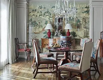 Dining room with chinoiserie wallpaper, crystal chandelier, and upholstered chairs around a round