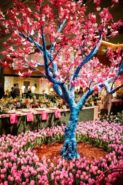 Blue tree with pink blossoms and butterflies surrounded by pink tulips