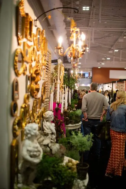 Ornate gold mirrors and cherub statues at a trade show with people browsing.