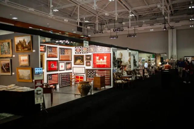 Show floor with booths displaying American flags, paintings, and antique furniture.