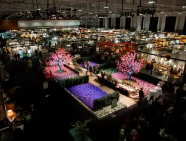 Indoor exhibition hall with booths, floral displays, and people browsing.