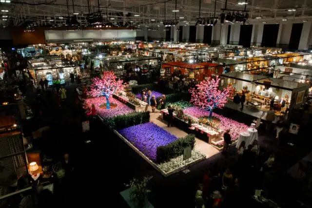 Indoor exhibition hall with booths, floral displays, and people browsing.