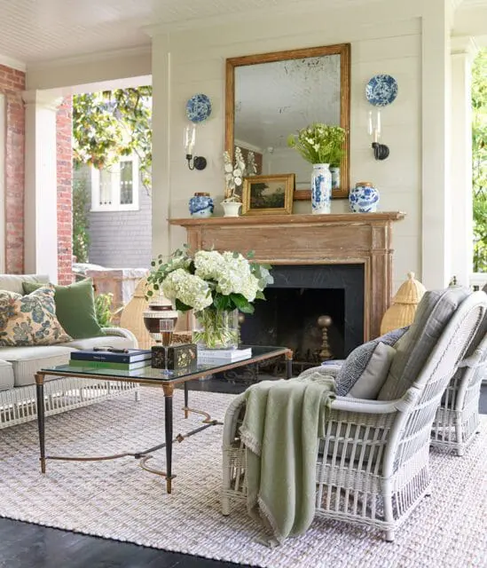 Porch living room with wicker furniture, fireplace, and floral arrangements.