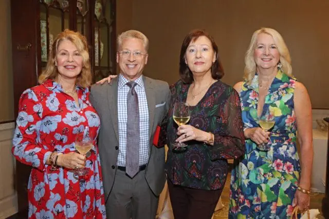 Four people smiling and holding wine glasses.