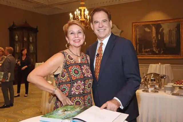 Man in suit and woman in colorful dress pose near a table with a book.