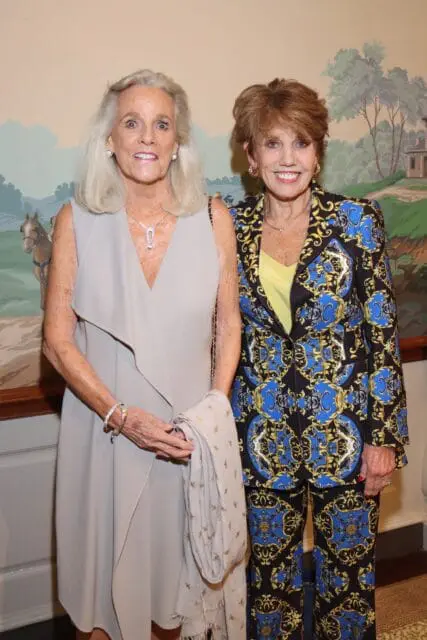 Two women posing in front of a mural. The woman on the left wears a beige dress and the woman on