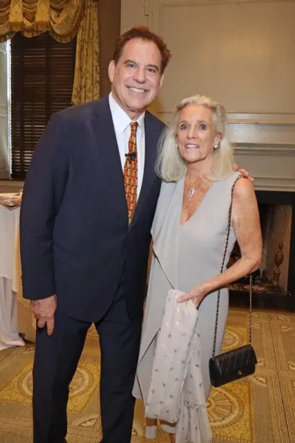 Man in navy suit and patterned tie with woman in light gray dress and black purse