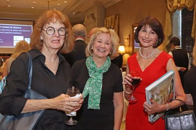 Three women at an event; one in black with glasses, one in black with green scarf, one in red