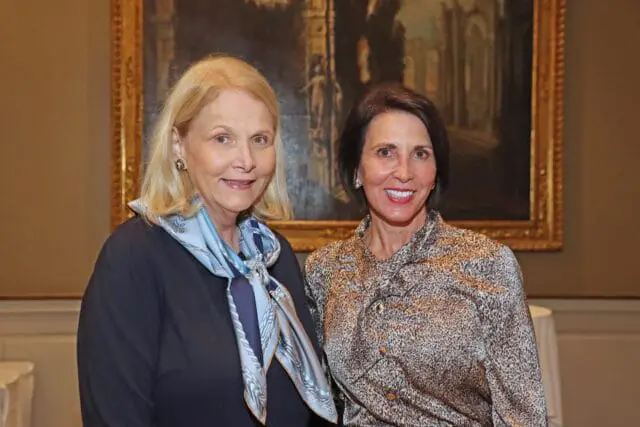 Two women smiling, one with blonde hair and a blue scarf, the other with dark hair and a leopard