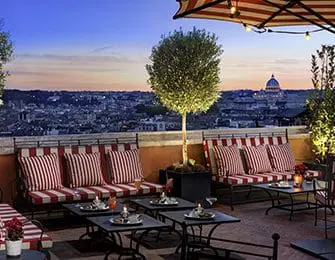 Outdoor seating area with tables, drinks, and a view of Rome.