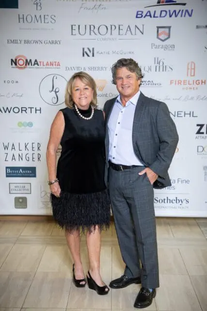 Man in a grey plaid suit and woman in a black feathered dress and pearl necklace