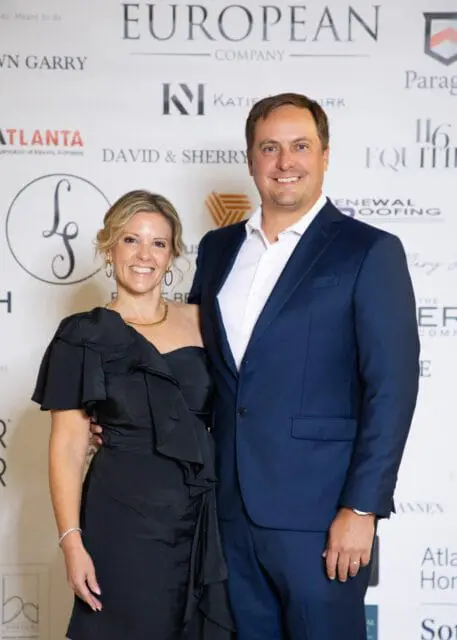 Couple posing for a photo in front of a backdrop with sponsor logos.