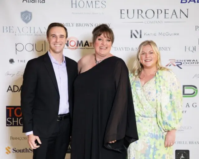 Three people smiling in front of a backdrop with sponsor logos.