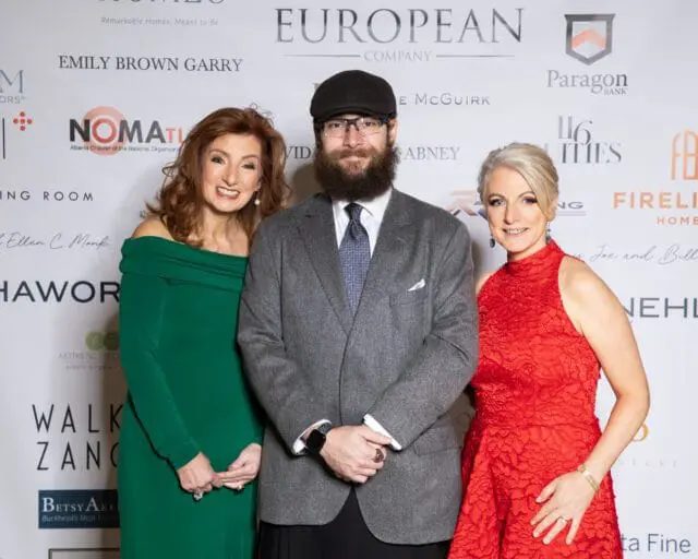 Three people posing for a photo in front of a branded backdrop
