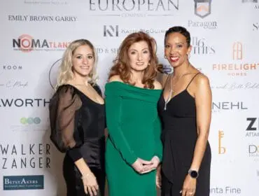Three women posing in front of a sponsor wall at an event.