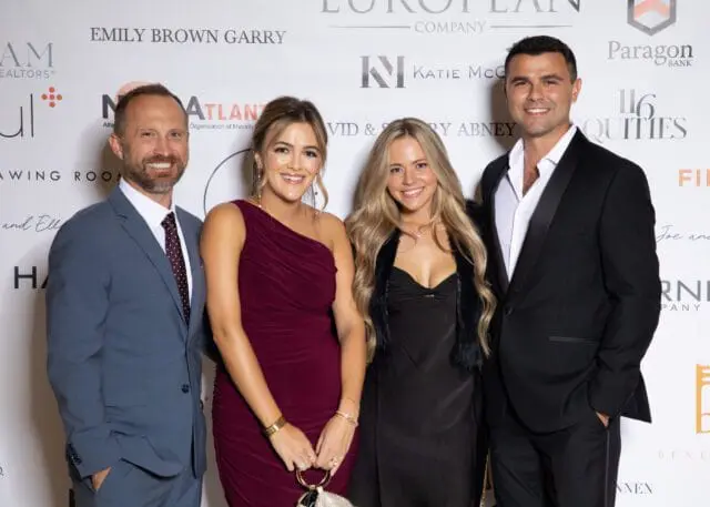 Four people posing for a photo in front of a backdrop with sponsor logos.