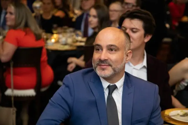 Man in blue suit and dark tie looking to the side at a formal event