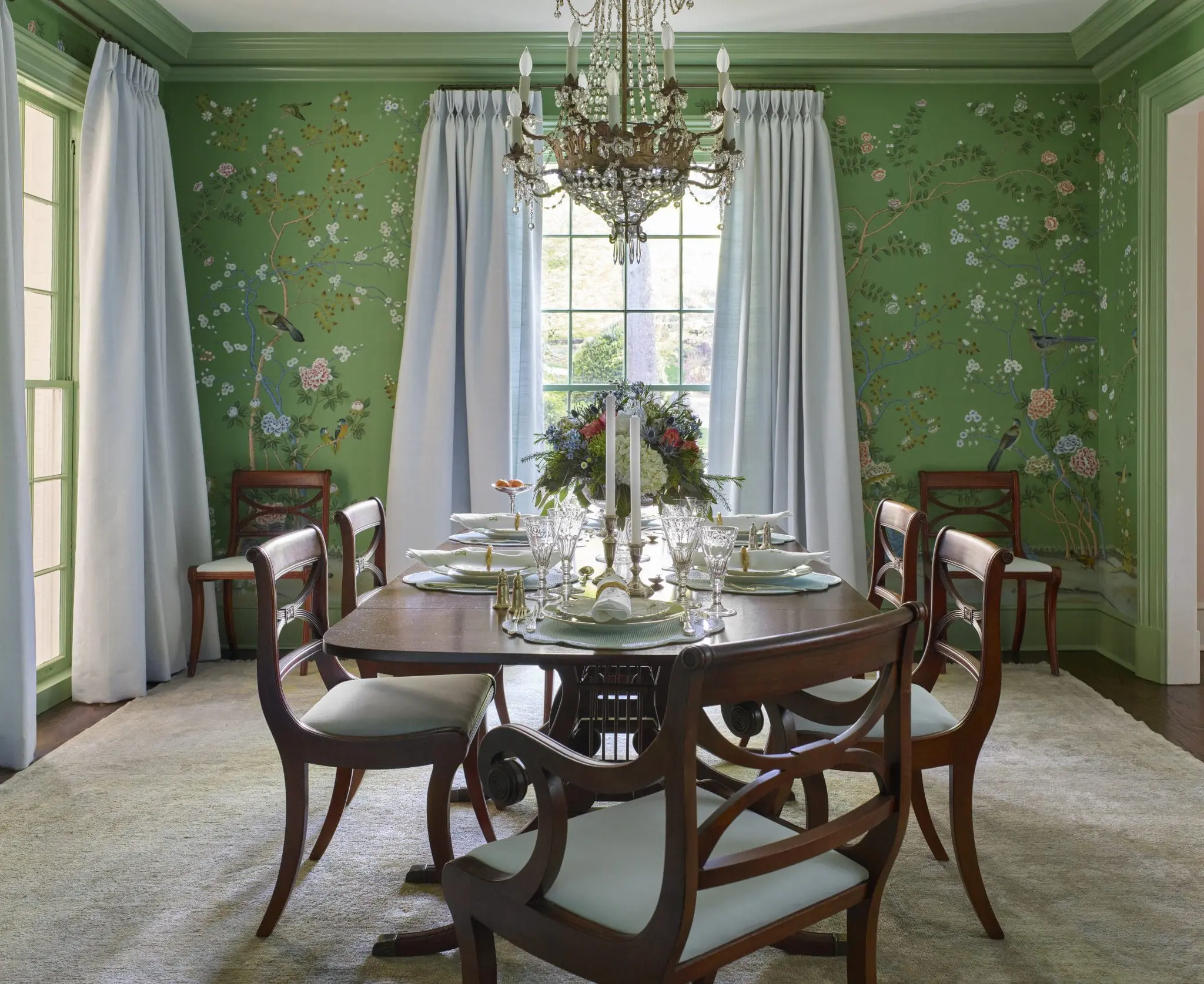 Dining room with green chinoiserie wallpaper, crystal chandelier, and formal table setting.