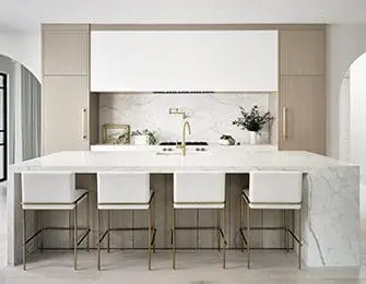 Modern kitchen with white marble island, light wood cabinetry, and brass hardware.