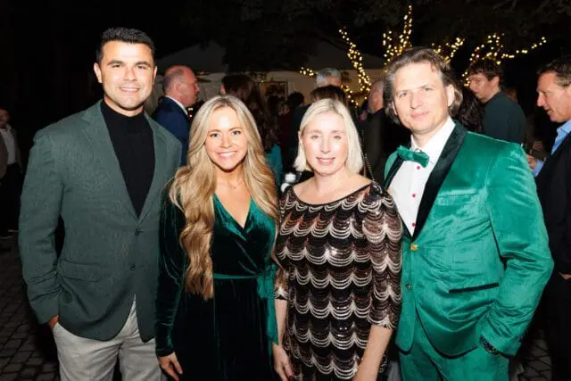 Four people posing for a photo at an outdoor event with string lights in the background.