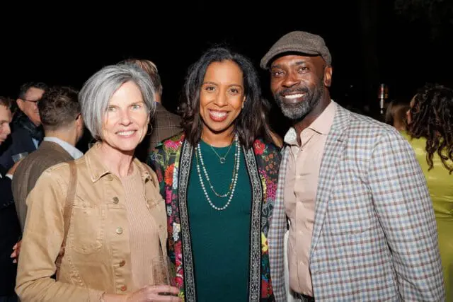 Three people smiling at the camera: a woman with gray hair, a woman in a colorful jacket, and a man